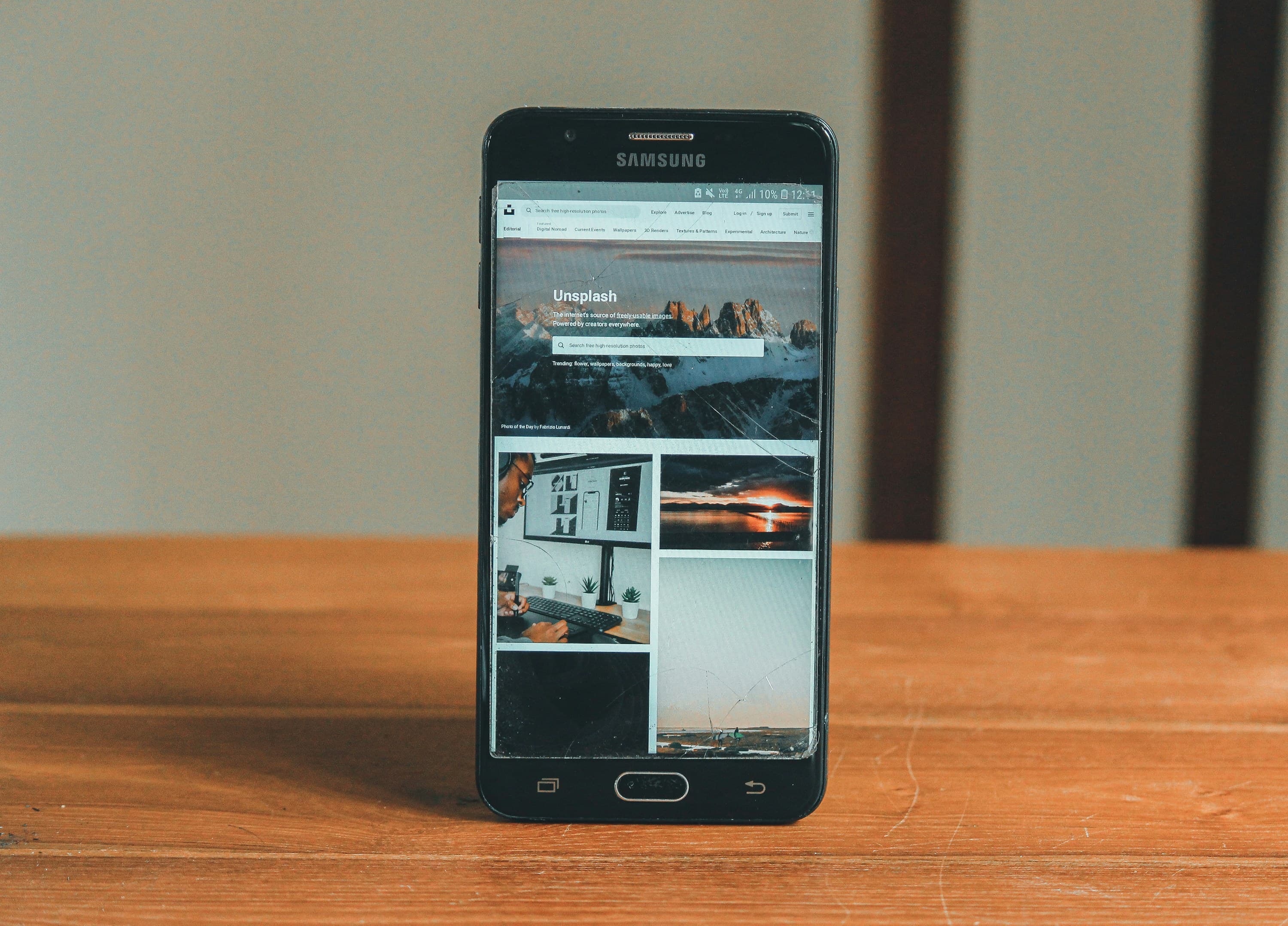 A black smartphone sits upright on a wooden table.